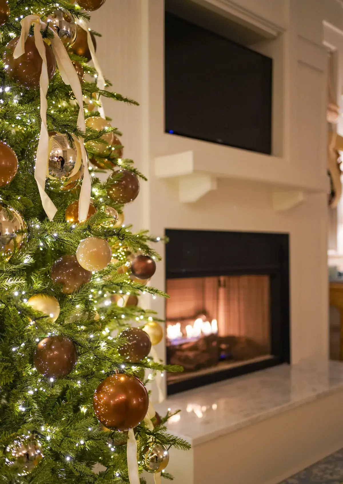 A Christmas tree with gold ornaments beside a lit fireplace