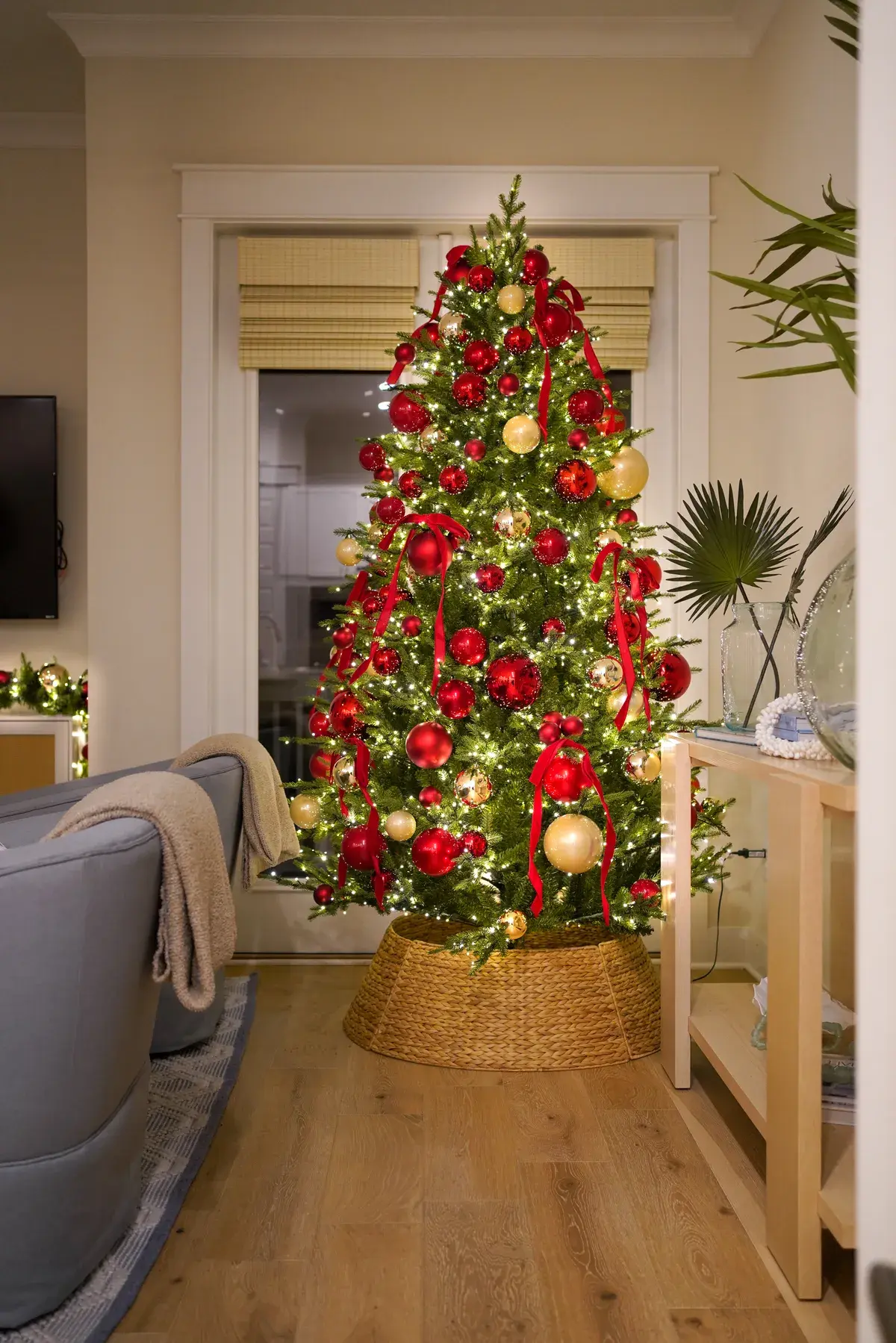 A Christmas tree with red ornaments in a woven tree collar